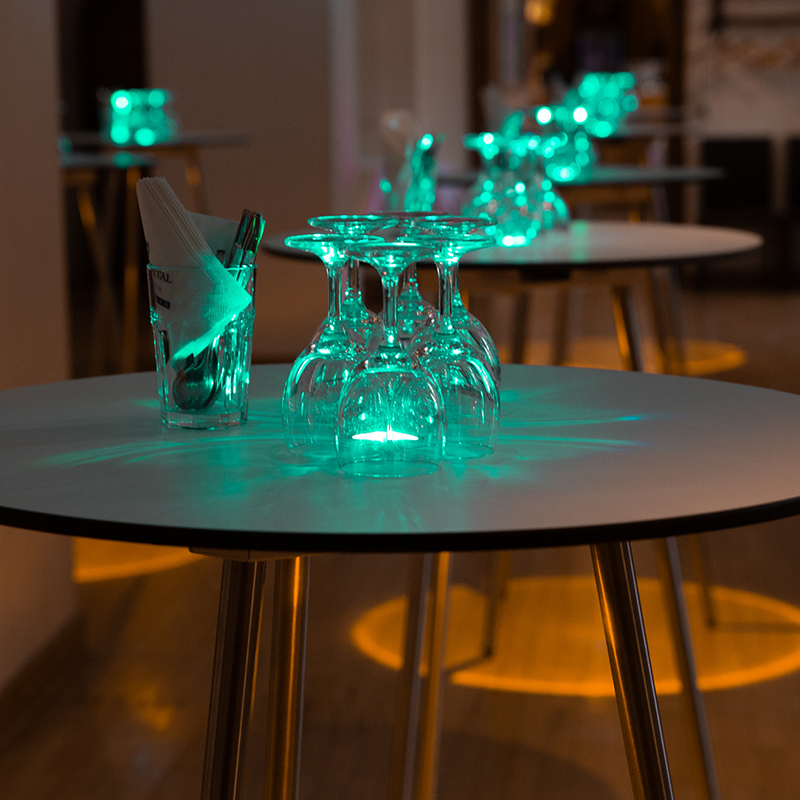 Stehtisch mit LED-Beleuchtung mieten zeigt runden Tisch mit leuchtenden Gläsern und Besteck in stilvoller Eventumgebung